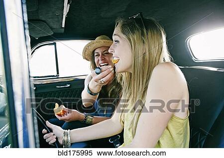 Stock Photography - Woman feeding friend in vintage car. Fotosearch