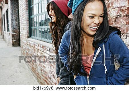 Stock Photograph - Women laughing in front of brick wall. Fotosearch