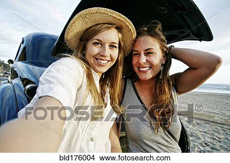 Picture - Women taking selfie in vintage car on beach. Fotosearch