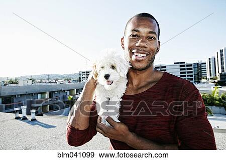 Stock Photo - African American man holding dog on urban rooftop. Fotosearch