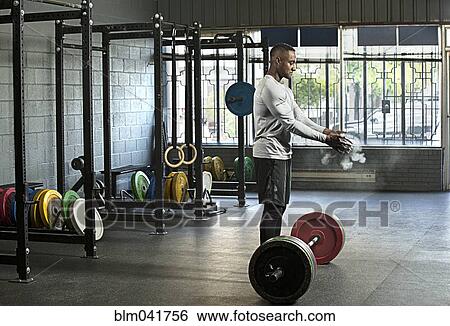 Stock Photograph - Black athlete chalking hands for weightlifting in gym. Fotosearch