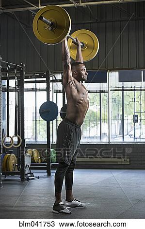 Stock Image - Black athlete lifting weights in gym. Fotosearch