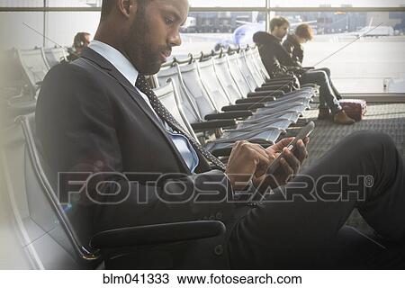 Stock Image - Black businessman using cell phone in airport. Fotosearch