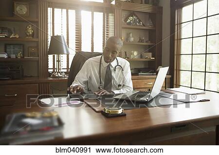 Stock Image - Black doctor using digital tablet in office. Fotosearch