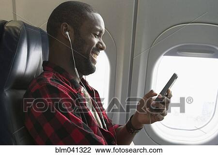 Stock Image - Black man listening to earbuds on airplane. Fotosearch