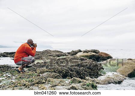 Stock Image - Black man photographing on beach. Fotosearch