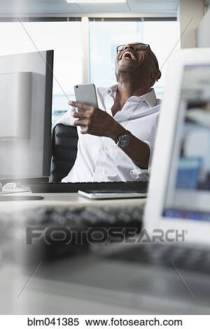 Businessman laughing at cell phone in office View Large Photo Image Stock Photography - Businessman laughing at cell phone in office. Fotosearch
