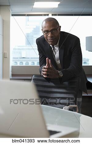 Businessman leaning on chair in office View Large Photo Image Stock Image - Businessman leaning on chair in office. Fotosearch