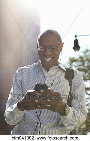 Stock Image - Businessman listening to earbuds outdoors. Fotosearch