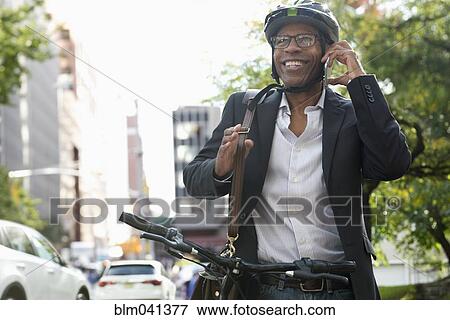 Stock Photo - Businessman talking on cell phone on bicycle. Fotosearch