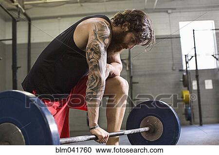 Stock Image - Caucasian athlete crouching at barbell in gym. Fotosearch