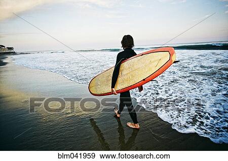 Caucasian man carrying surfboard at beach View Large Photo Image Stock Photo - Caucasian man carrying surfboard at beach. Fotosearch