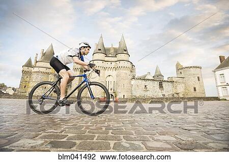 Stock Image - Caucasian man cycling near castle. Fotosearch