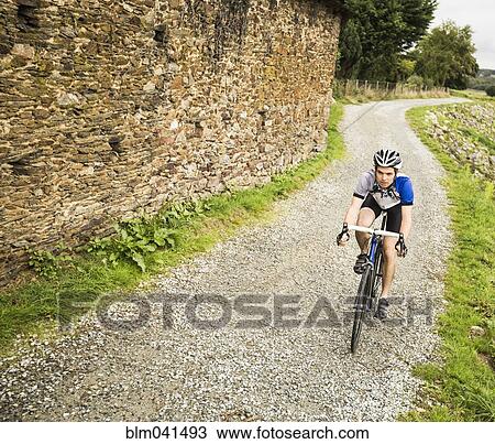 Stock Image - Caucasian man cycling on gravel path. Fotosearch