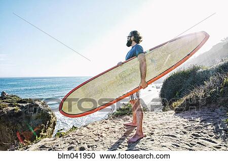 Stock Image - Caucasian man holding surfboard at beach. Fotosearch