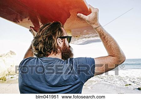 Stock Image - Caucasian man holding surfboard at beach. Fotosearch