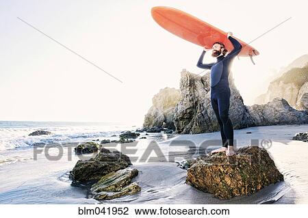 Stock Image - Caucasian man holding surfboard at beach. Fotosearch