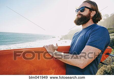 Stock Photo - Caucasian man holding surfboard at beach. Fotosearch