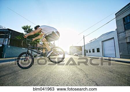 Stock Image - Caucasian man jumping on BMX bike on street. Fotosearch