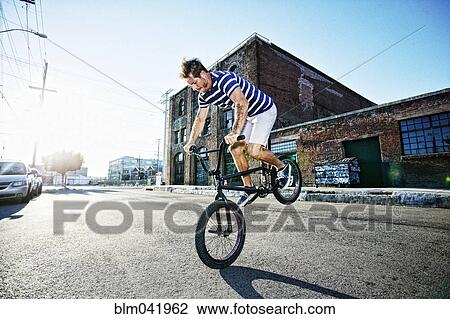Stock Image - Caucasian man riding BMX bike on street. Fotosearch