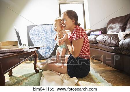 Stock Photography - Caucasian mother and baby daughter using laptop in living room. Fotosearch