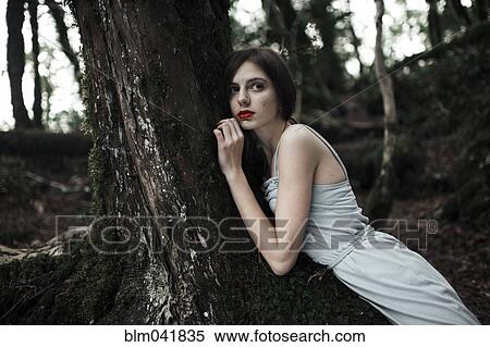 Stock Photography - Caucasian woman leaning on tree in forest. Fotosearch