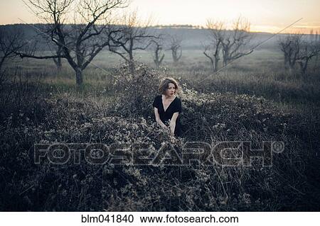 Stock Image - Caucasian woman sitting in remote field. Fotosearch