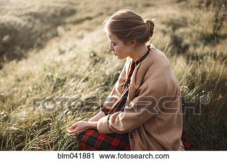 Stock Image - Caucasian woman sitting in remote field. Fotosearch