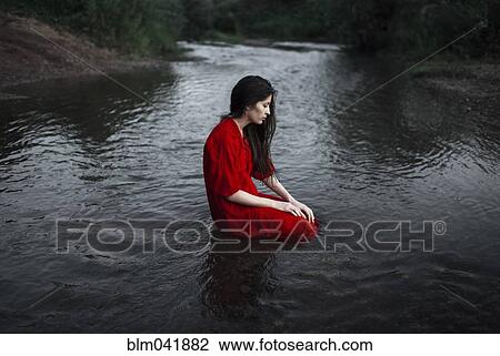 Stock Image - Caucasian woman sitting in remote stream. Fotosearch