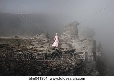Stock Image - Caucasian woman standing on misty rock formation. Fotosearch