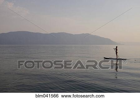 Stock Photograph - Caucasian woman standing on paddleboard in lake. Fotosearch