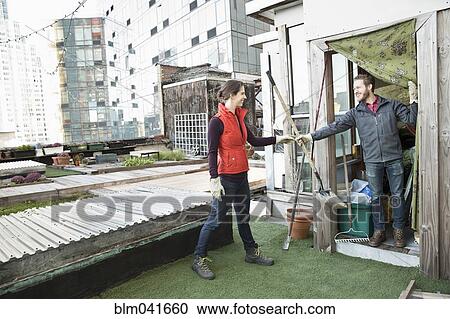Stock Image - Couple holding gardening tools on urban rooftop. Fotosearch