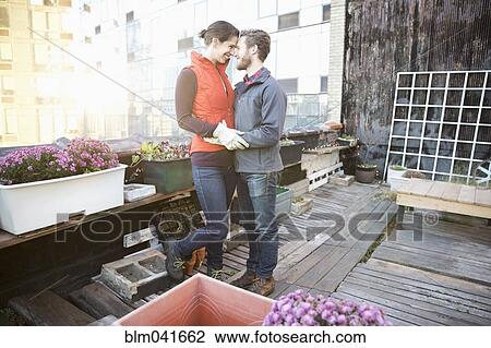 Stock Image - Couple hugging in urban rooftop garden. Fotosearch