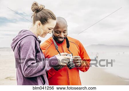 Couple reviewing digital photographs on beach View Large Photo Image Stock Photograph - Couple reviewing digital photographs on beach. Fotosearch