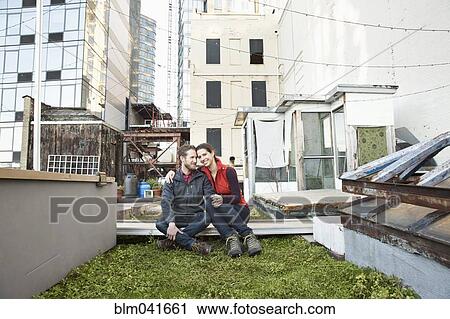 Stock Image - Couple smiling in urban rooftop garden. Fotosearch