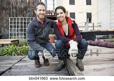 Stock Image - Couple smiling in urban rooftop garden. Fotosearch