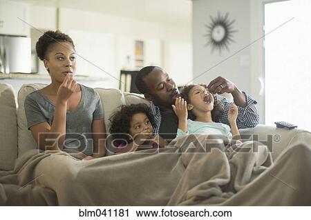 Stock Image - Family in blanket snacking on sofa. Fotosearch