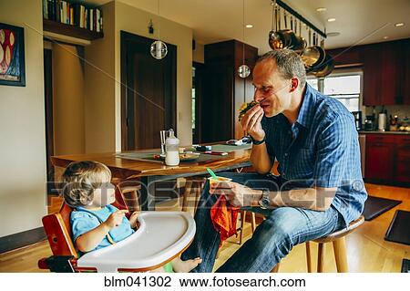 Father feeding baby son in high chair View Large Photo Image Stock Image - Father feeding baby son in high chair. Fotosearch