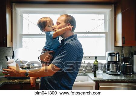 Stock Image - Father kissing baby son in kitchen. Fotosearch