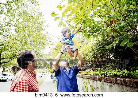 Stock Photograph - Father lifting baby son to tree branches. Fotosearch