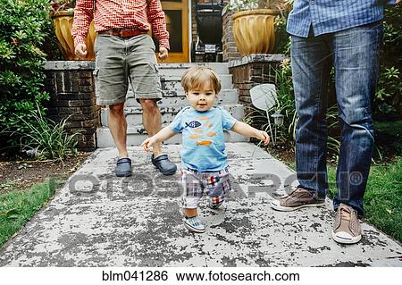 Stock Photograph - Gay fathers and baby son standing outdoors. Fotosearch