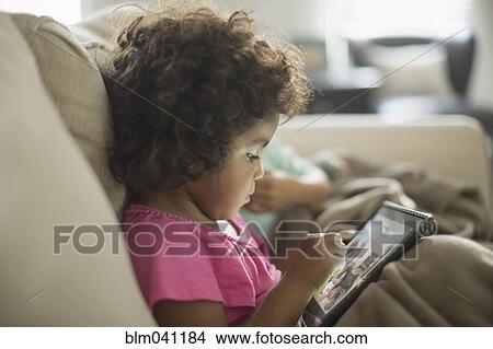 Picture - Girl using digital tablet on sofa. Fotosearch