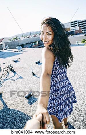 Picture - Hispanic woman pulling hand on urban rooftop. Fotosearch