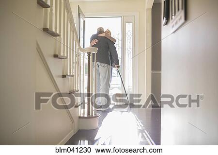 Stock Image - Man hugging visitor in front door. Fotosearch