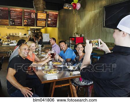 Stock Photograph - Man photographing friends in cafe. Fotosearch