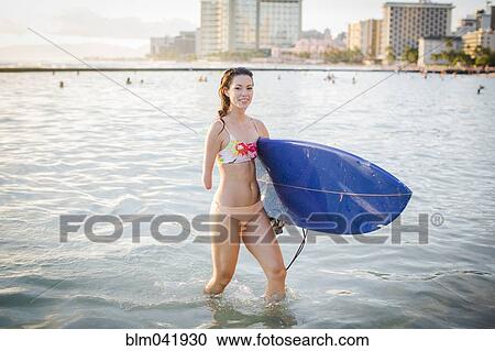 Stock Image - Mixed race amputee carrying surfboard in ocean. Fotosearch