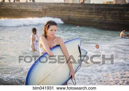 Stock Image - Mixed race amputee carrying surfboard on beach. Fotosearch