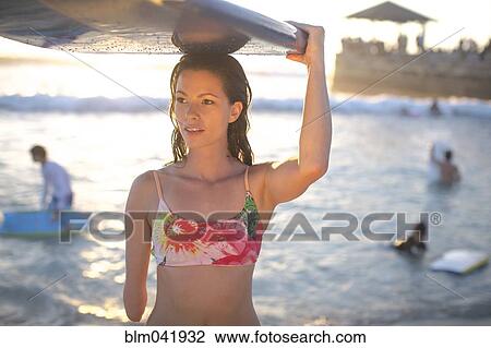 Stock Image - Mixed race amputee carrying surfboard on beach. Fotosearch