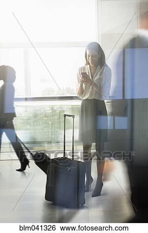 Stock Photograph - Mixed race businesswoman using cell phone in airport. Fotosearch