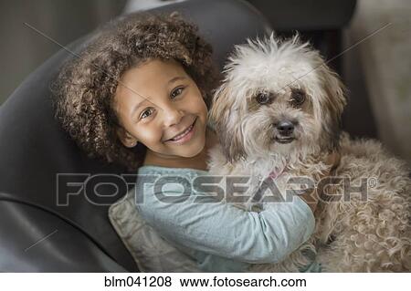 Stock Photo - Mixed race girl petting dog on sofa. Fotosearch